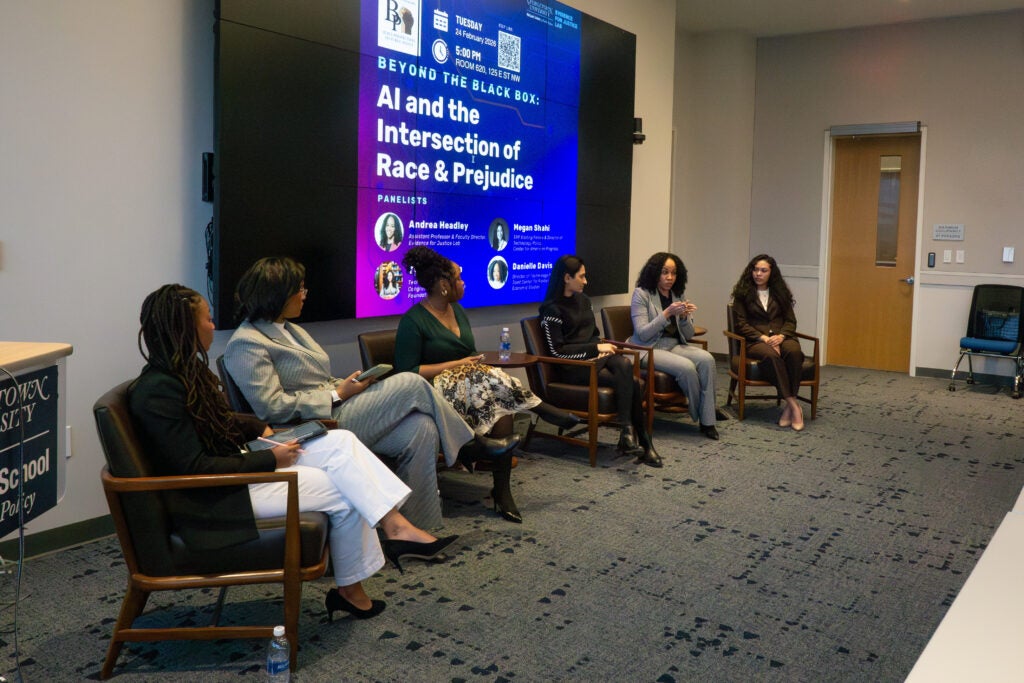 black box expert panel from the left peripheral side. Slideshow behind speakers read AI and the Intersection of Race and Prejudice